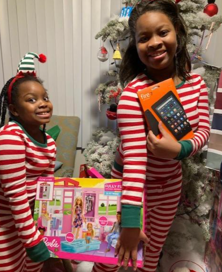 Two excited kids in striped pajamas hold gifts in front of a Christmas tree